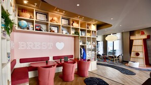 A modern interior with a red and white color scheme, featuring a seating area with red chairs and a bench, a bookshelf with various items, and a wall with the word "BREST" and a heart symbol. - ibis Budget Brest Centre Port (Brest)