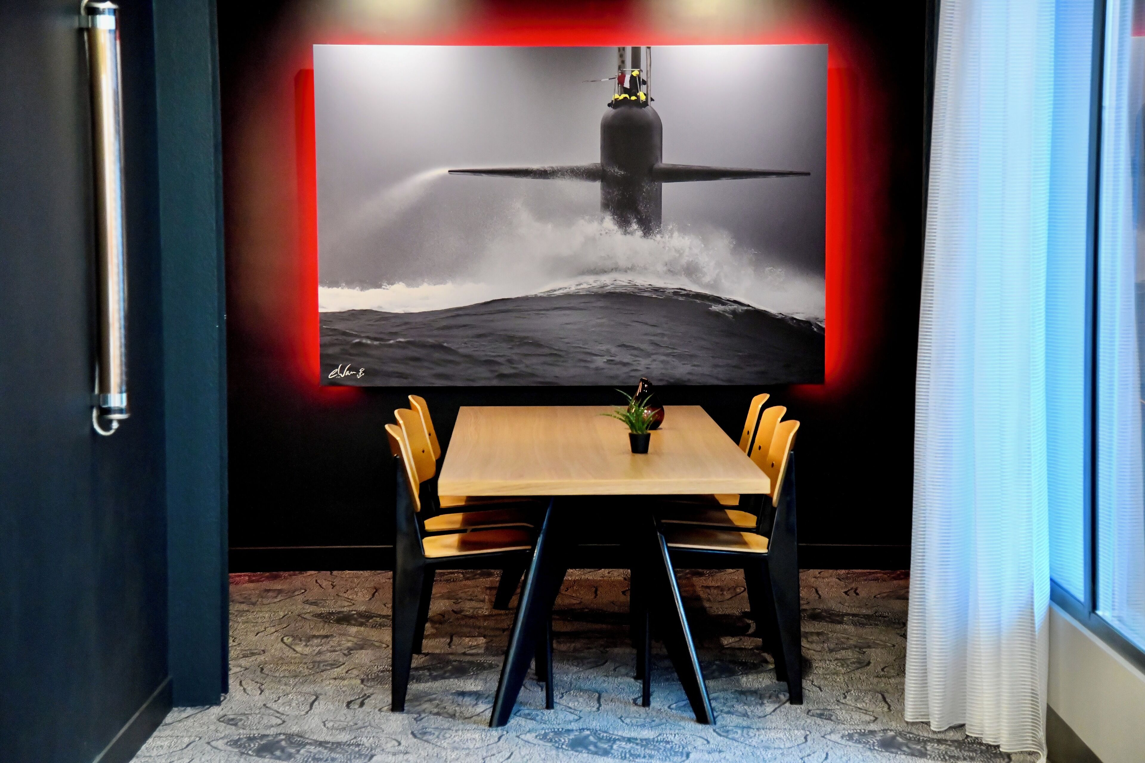 A room with a wooden table and chairs, a potted plant, and a large framed picture of a submarine.