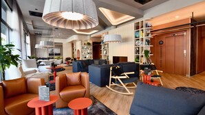 A modern hotel lobby with leather sofas, red tables, and a large bookshelf. - ibis Budget Brest Centre Port (Brest)