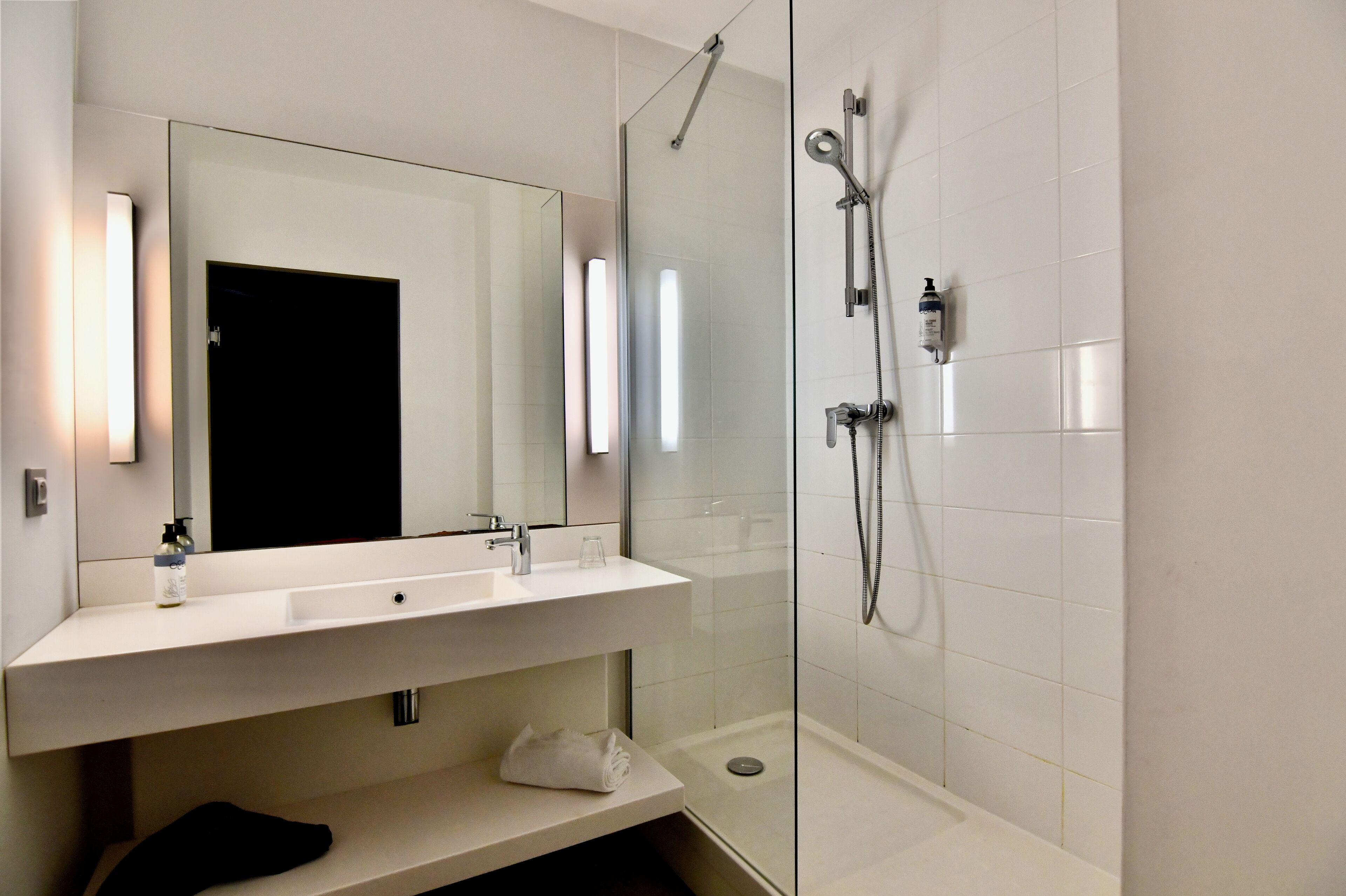 Un baño moderno con ducha separada por vidrio, un espejo grande y un lavabo blanco.