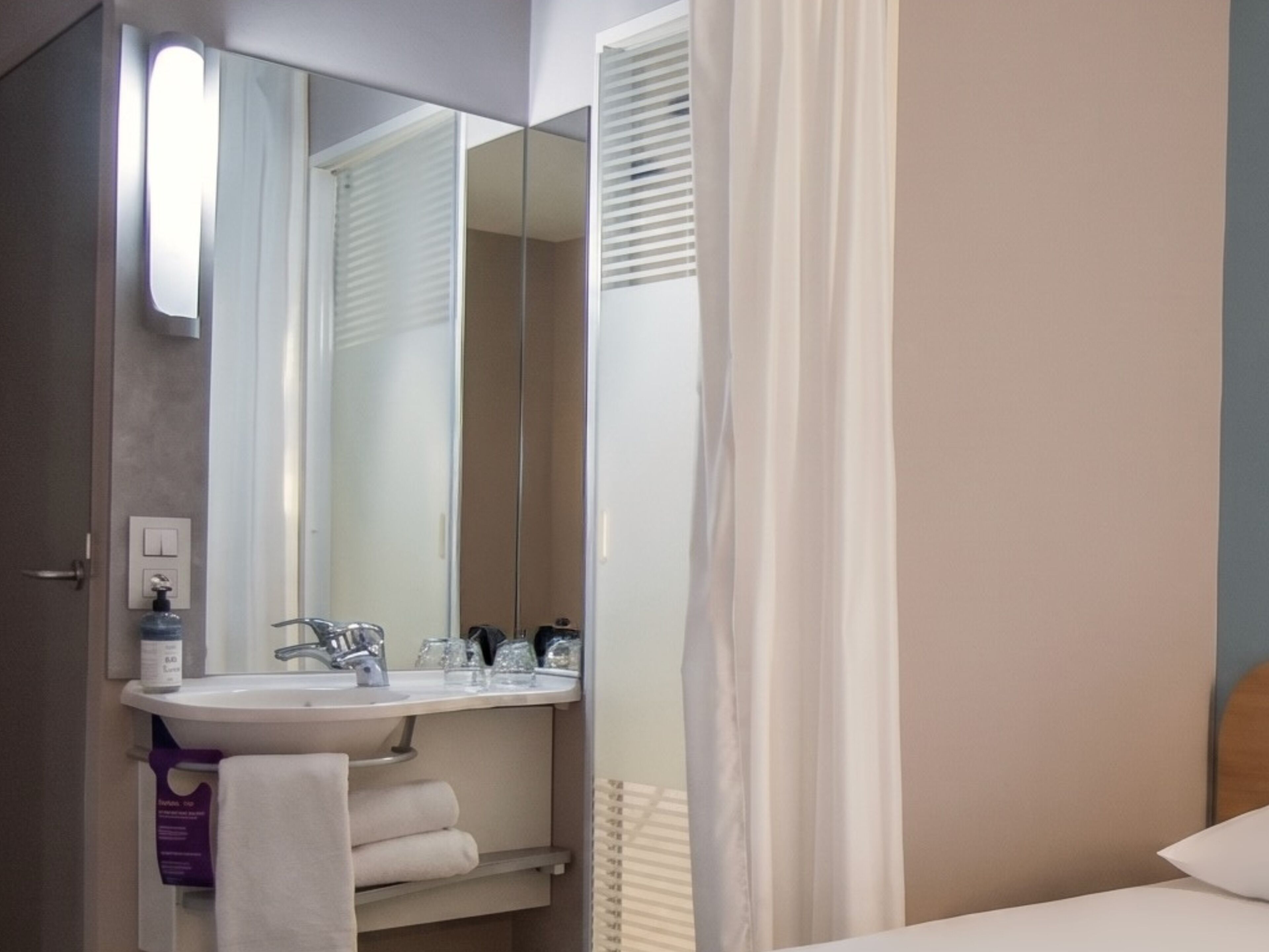 Ein Badezimmer mit Waschbecken, Spiegel, Handtuchhalter und einem Bett mit Kopfteil.
