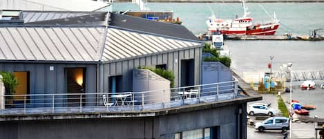 Un edificio moderno con balcón que da a un puerto deportivo con barcos.