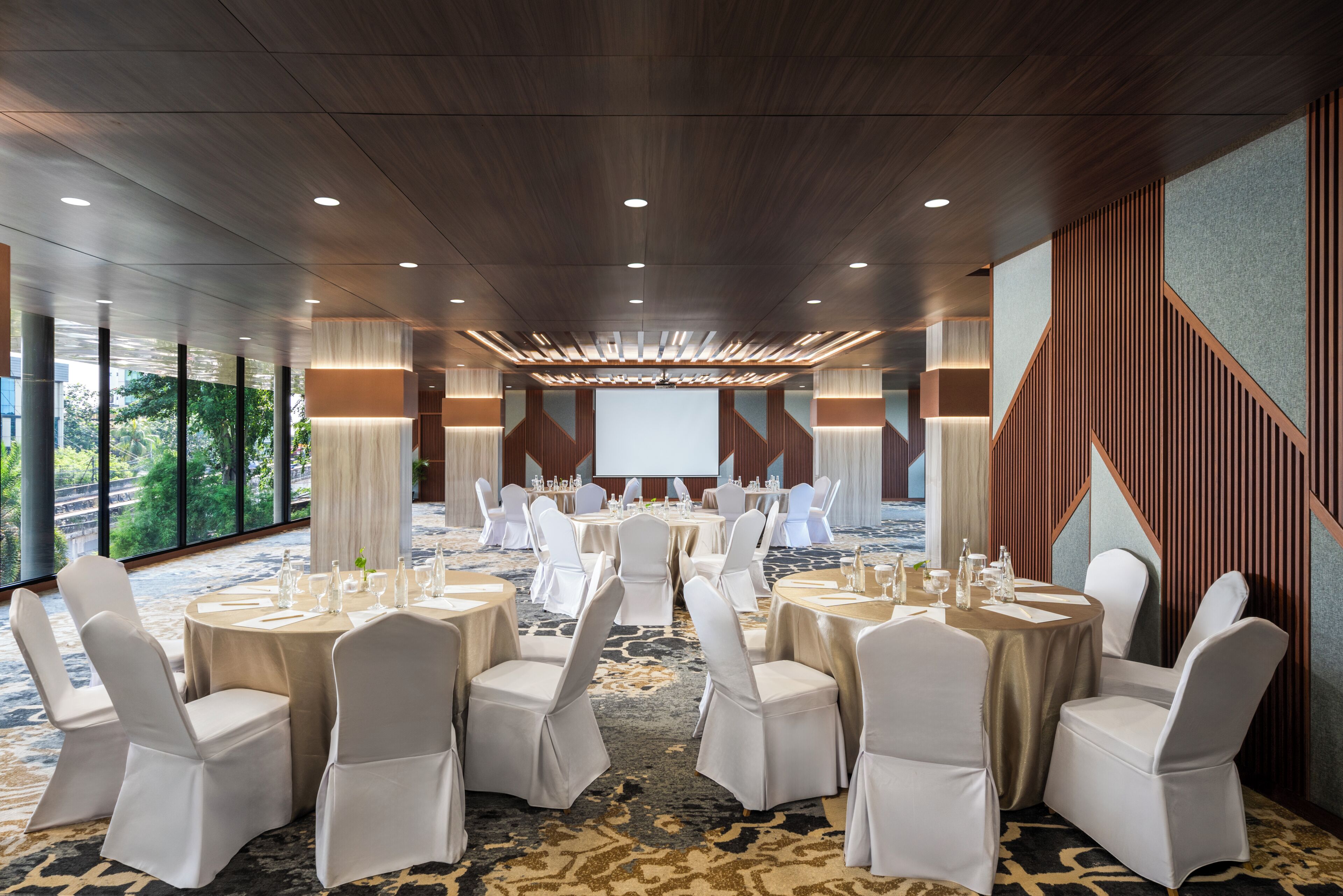A conference room with round tables, white chairs, and a large screen at the front.