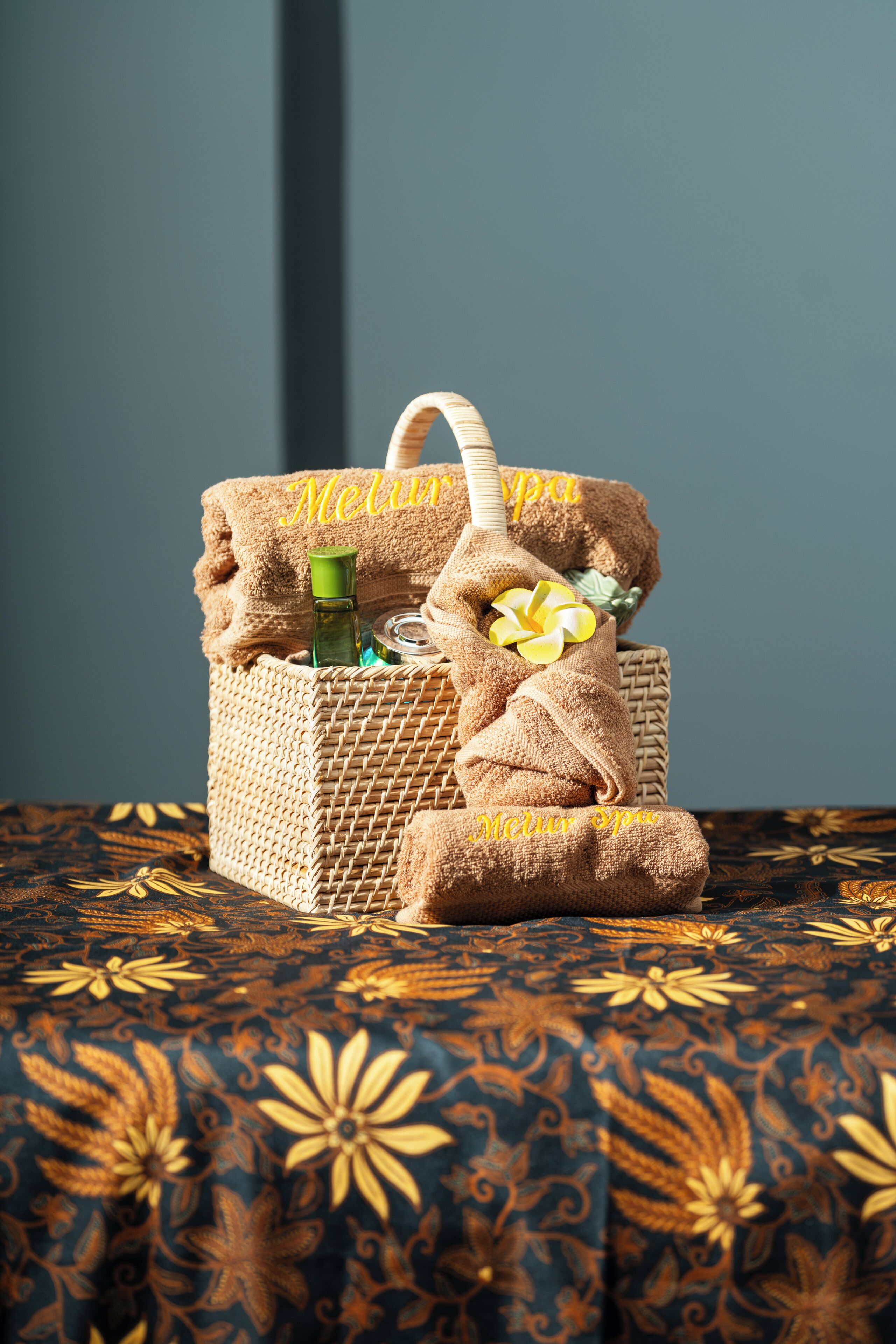 Un panier tressé contenant une serviette et une bouteille verte, posé sur une nappe à motifs.