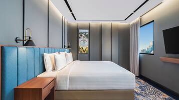 Habitación de hotel moderna con una cama grande, una mesita de noche de madera, un televisor de pantalla plana y vistas a la ciudad.
