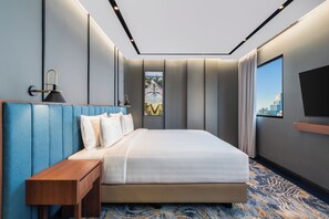 Quarto de hotel moderno com uma cama grande, mesa de cabeceira de madeira, televisão de tela plana e vista para a cidade.