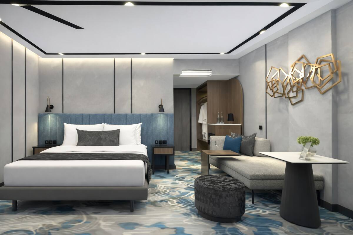 A modern hotel room with a large bed, a sofa, a small table, and a decorative wall piece.