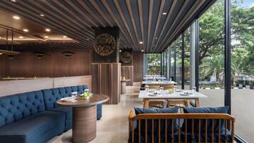 A modern restaurant interior with a blue sofa, round tables, and a view of the outdoors.