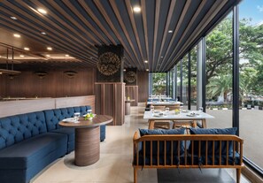 Interior moderno de restaurante com um sofá azul, mesas redondas e vista para o exterior.