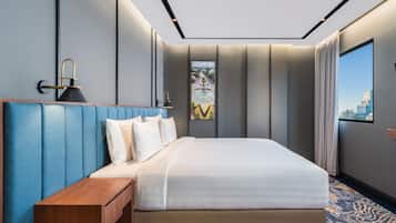 A modern hotel room with a large bed, a wooden nightstand, a city view through a window, and a patterned carpet.