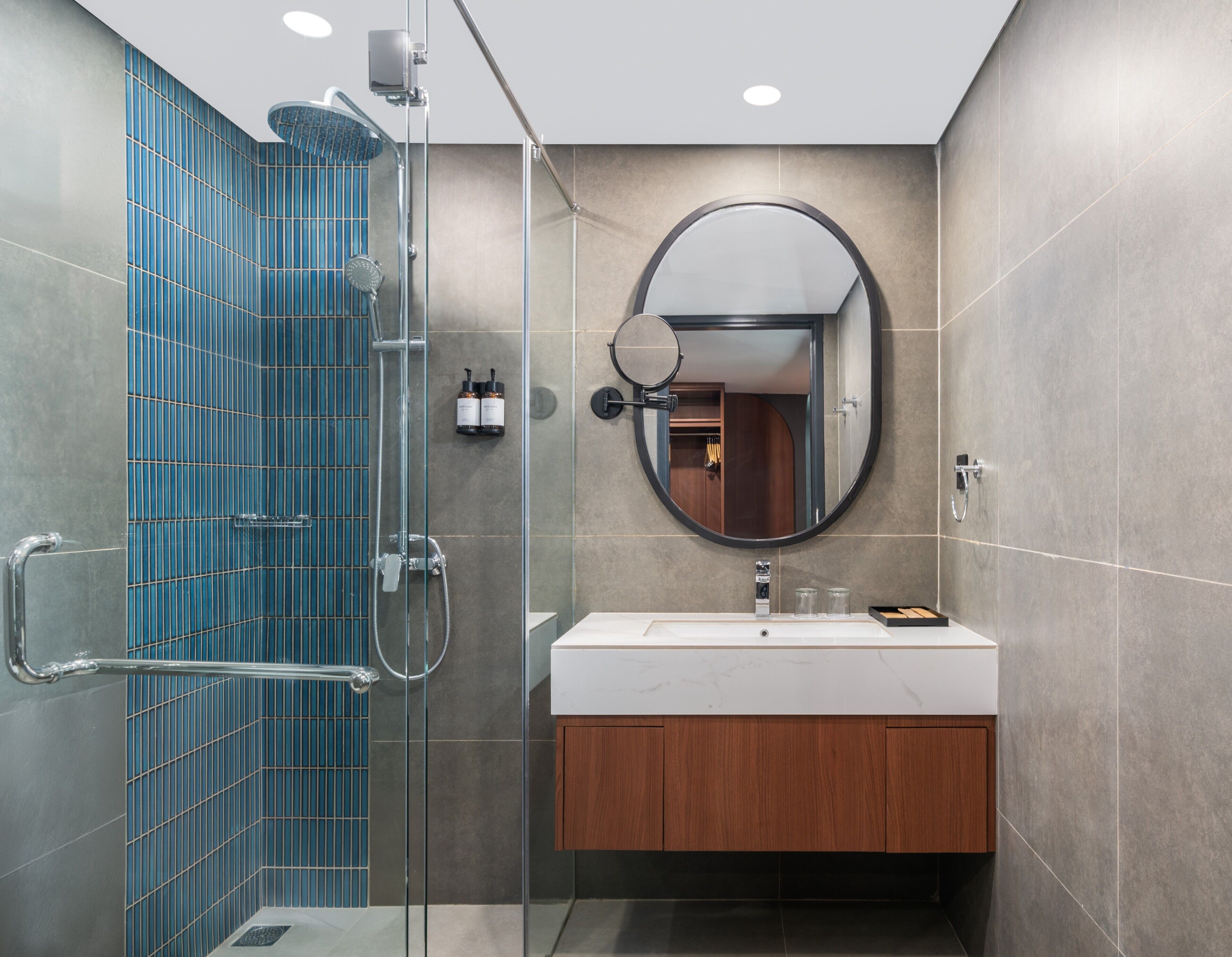 A modern bathroom with a glass-enclosed shower, a round mirror, and a wooden vanity.