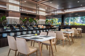 Um restaurante moderno com um balcão comprido, várias áreas de estar e vista para o verde lá fora.