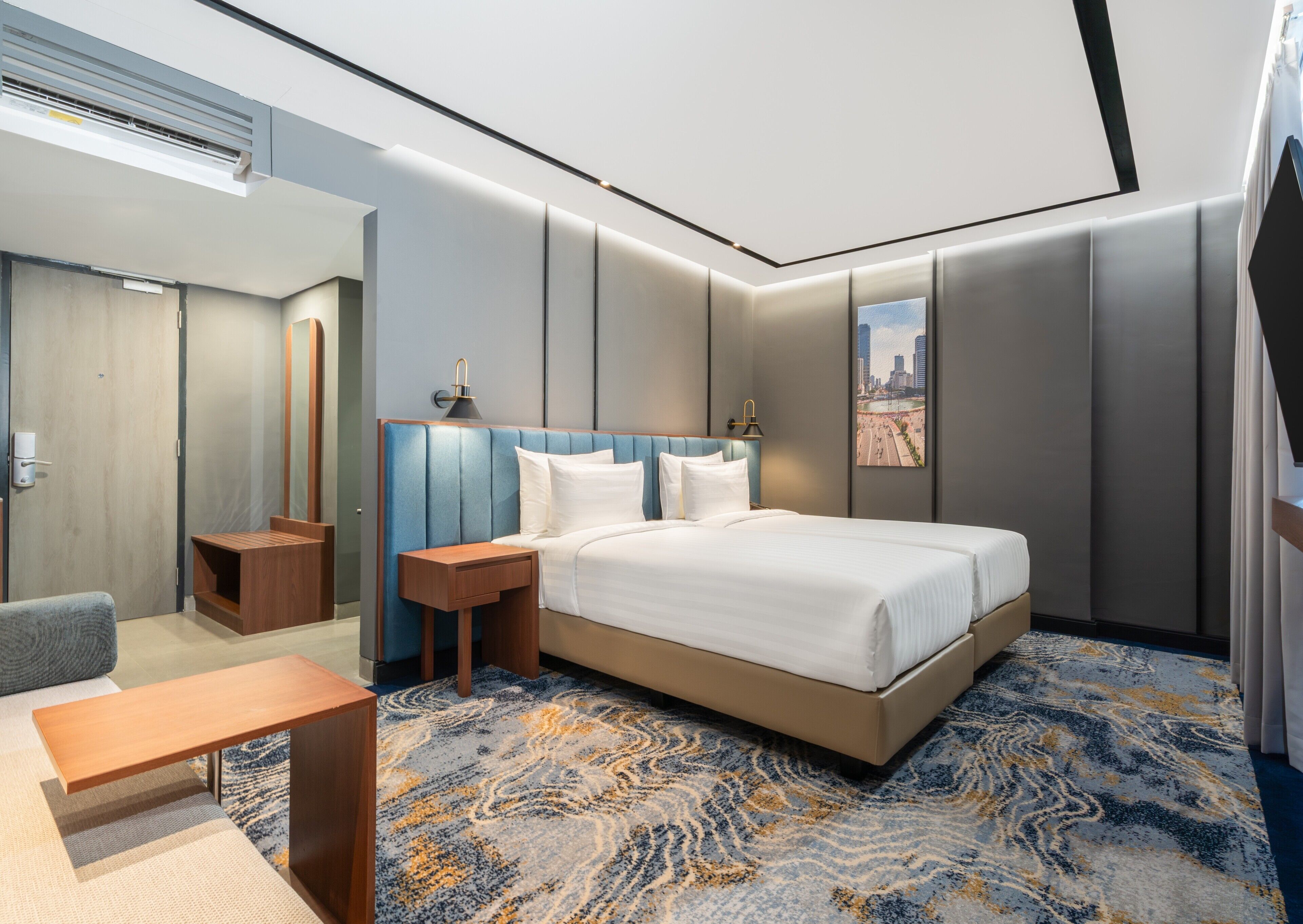 A modern hotel room with a large bed, a bedside table, a chair, and a cityscape view.