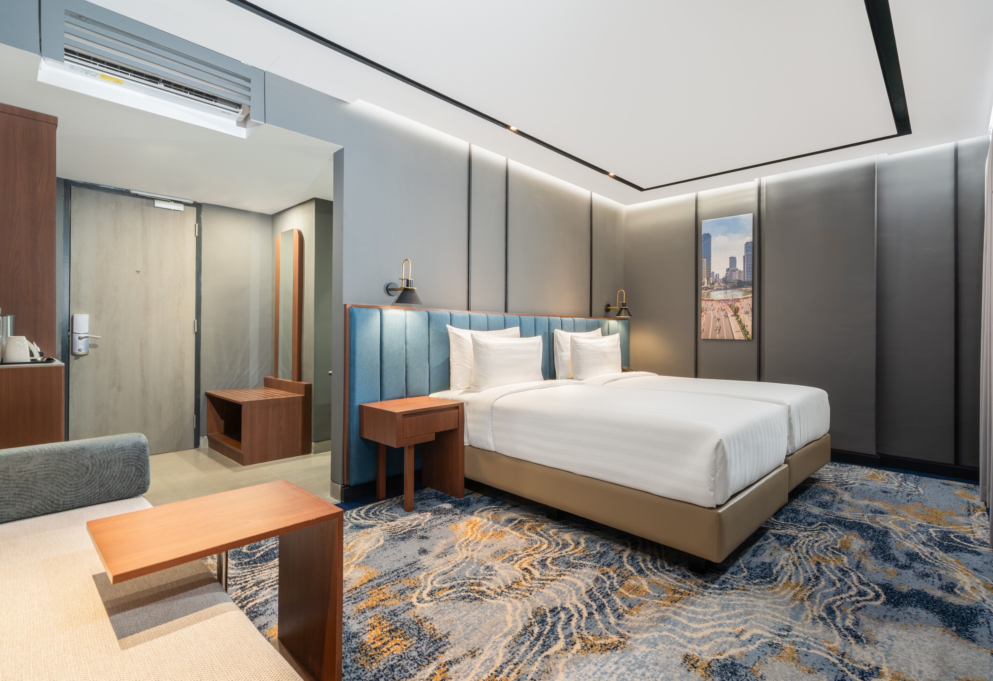 Una moderna camera d'hotel con un letto, comodini, una scrivania, una sedia, uno specchio e vista sulla città.