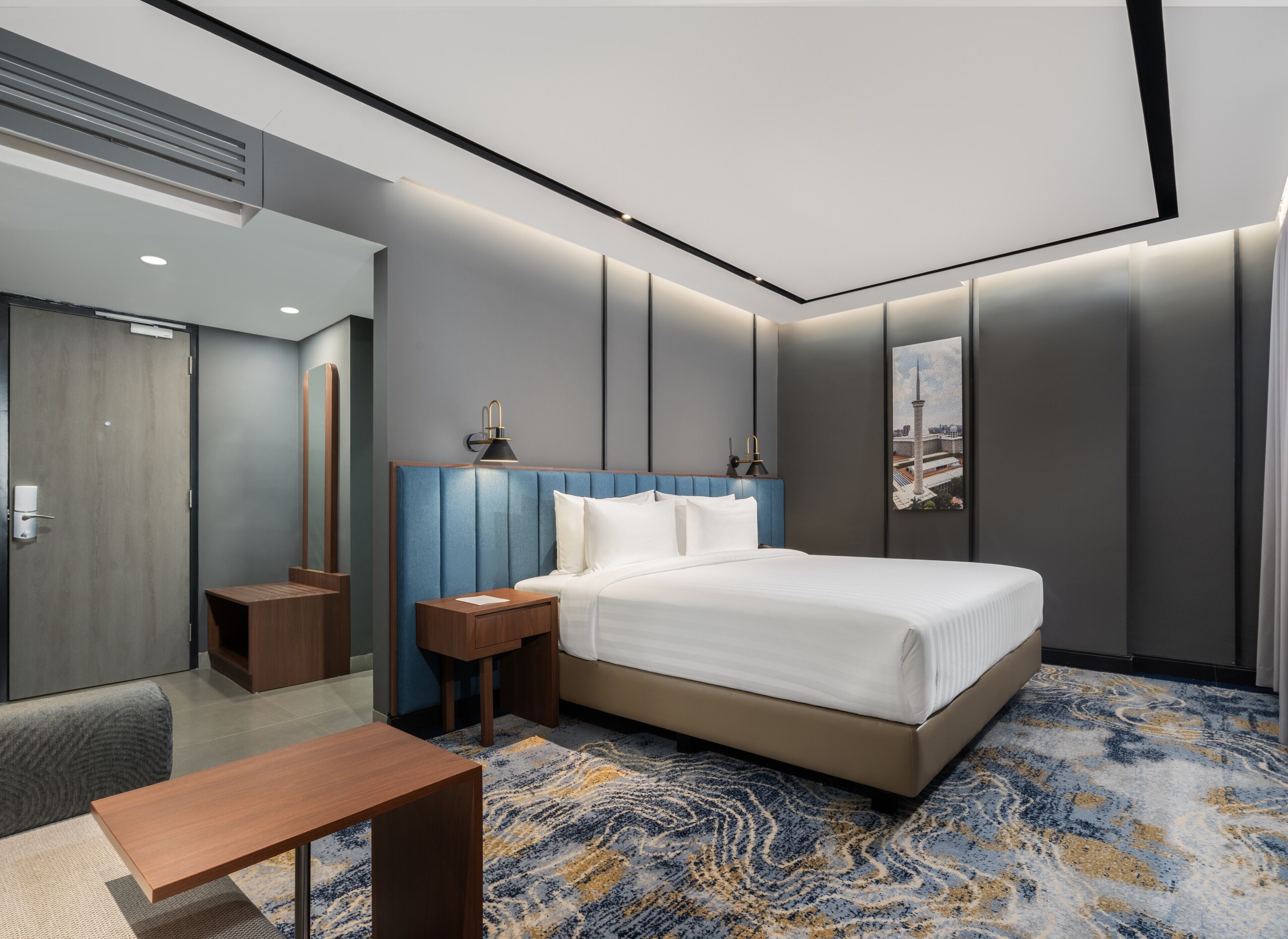 A modern hotel room with a large bed, bedside tables, a desk, and a view of a cityscape.