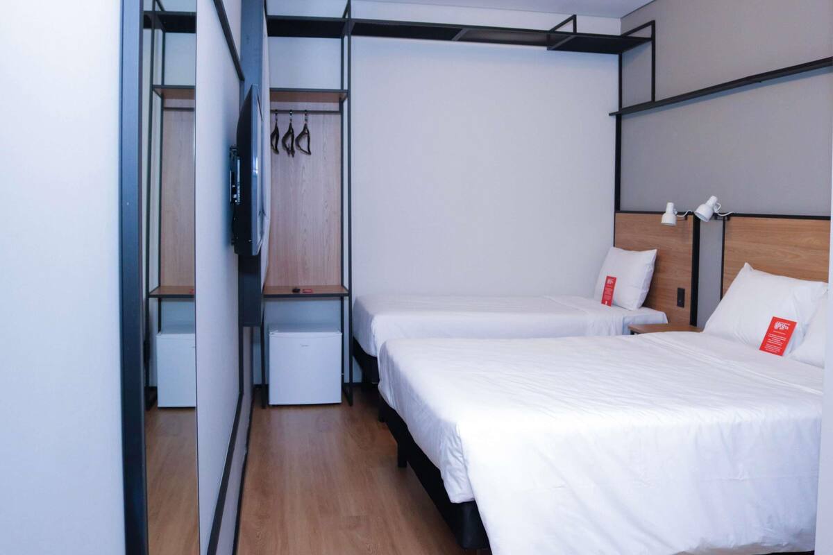 A hotel room with two beds, a wardrobe, and a small desk.