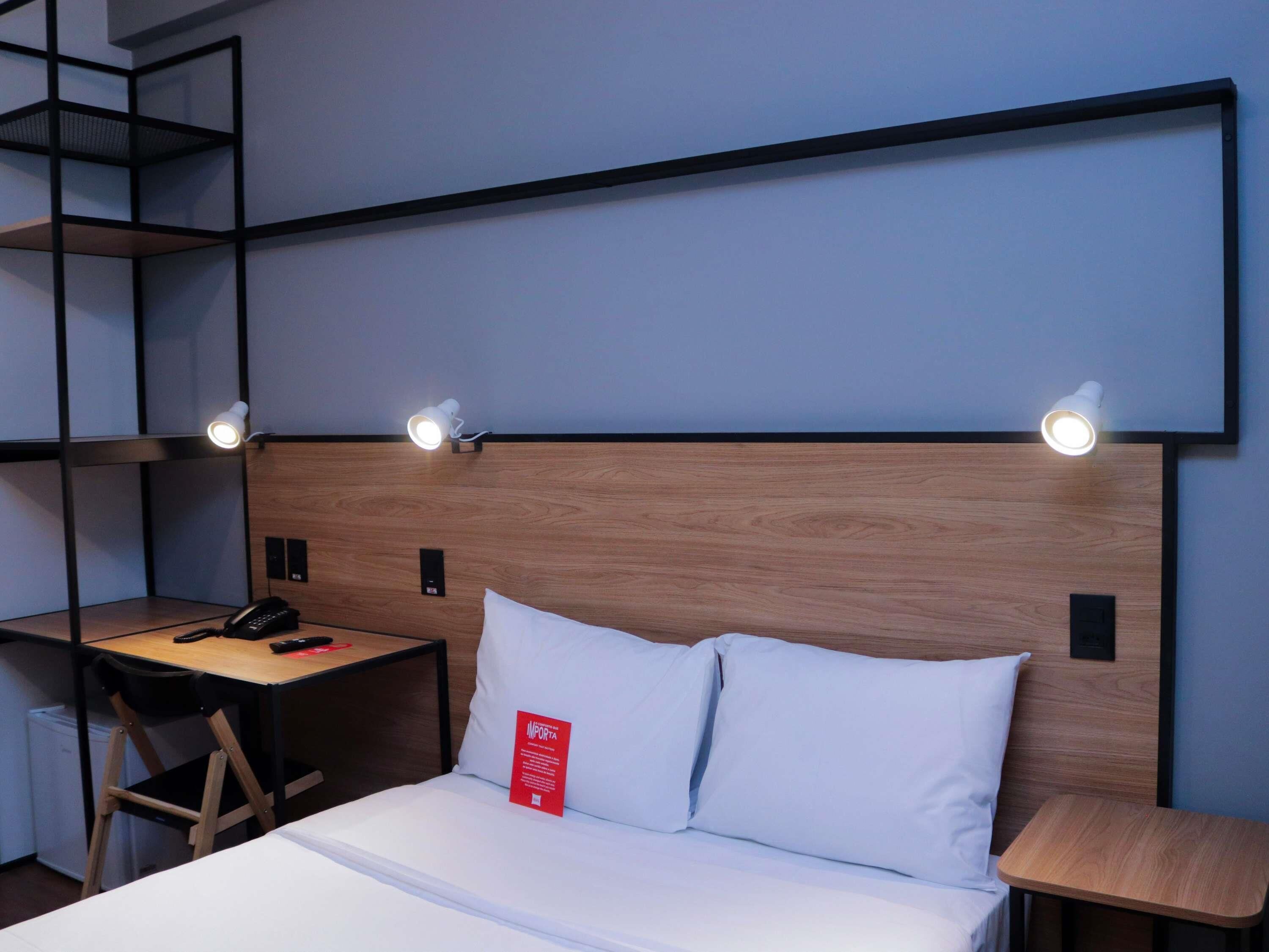 Ein Hotelzimmer mit einem Bett, einem Schreibtisch, einem Stuhl, einem kleinen Tisch und einem Wandregal.