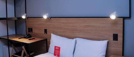 Ein Hotelzimmer mit einem Bett, einem Schreibtisch, einem Stuhl, einem kleinen Tisch und einem Wandregal.