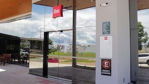 A modern building entrance with a glass facade, a red sign with 'ibis' logo, and a no parking sign. - ibis Primavera Do Leste (Primavera do Leste)