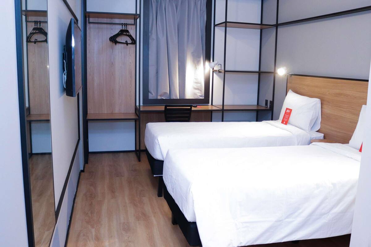 A compact hotel room with two single beds, a desk with a chair, a wardrobe, and a TV.