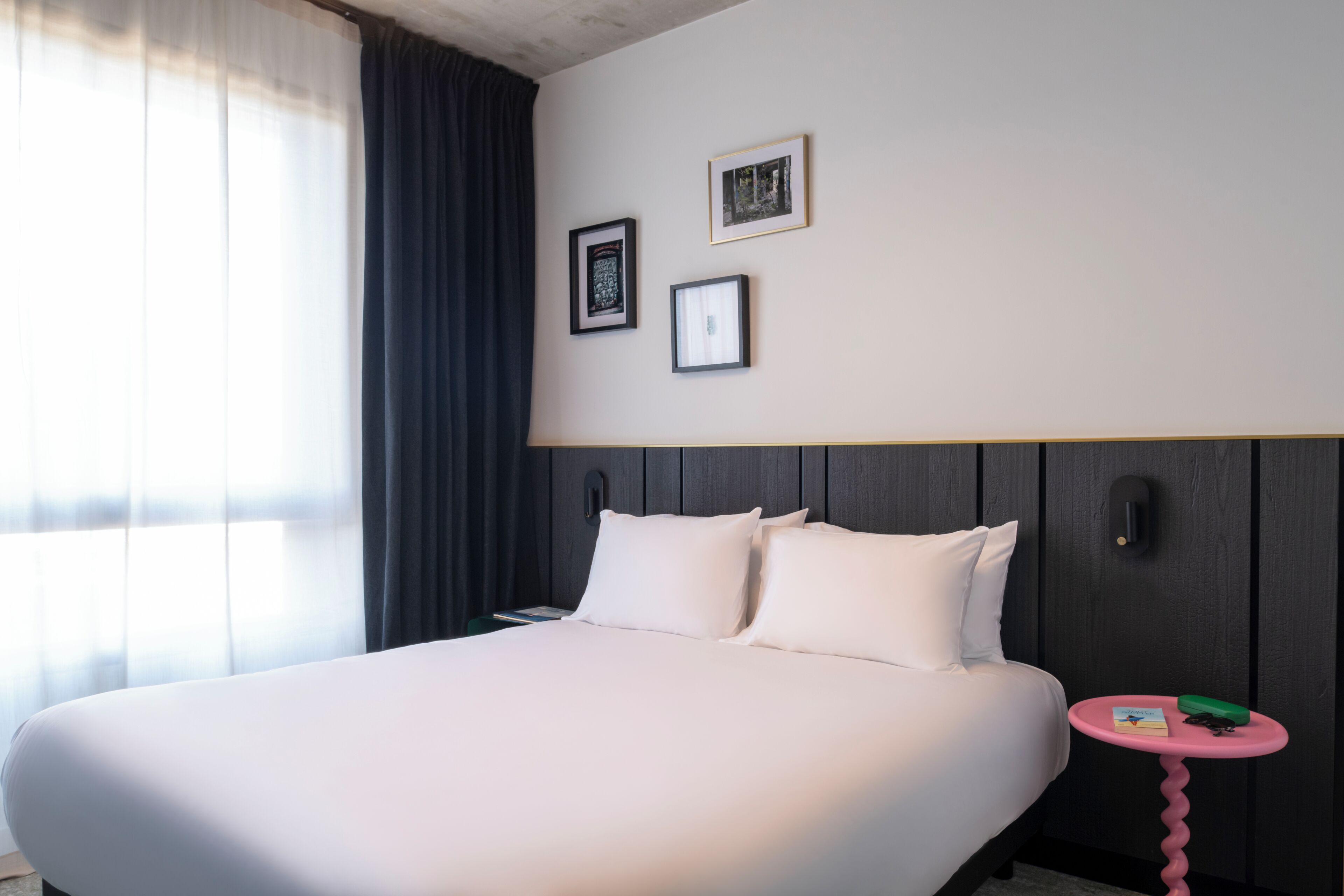 A hotel room with a large bed, a small round table, and two framed pictures on the wall.