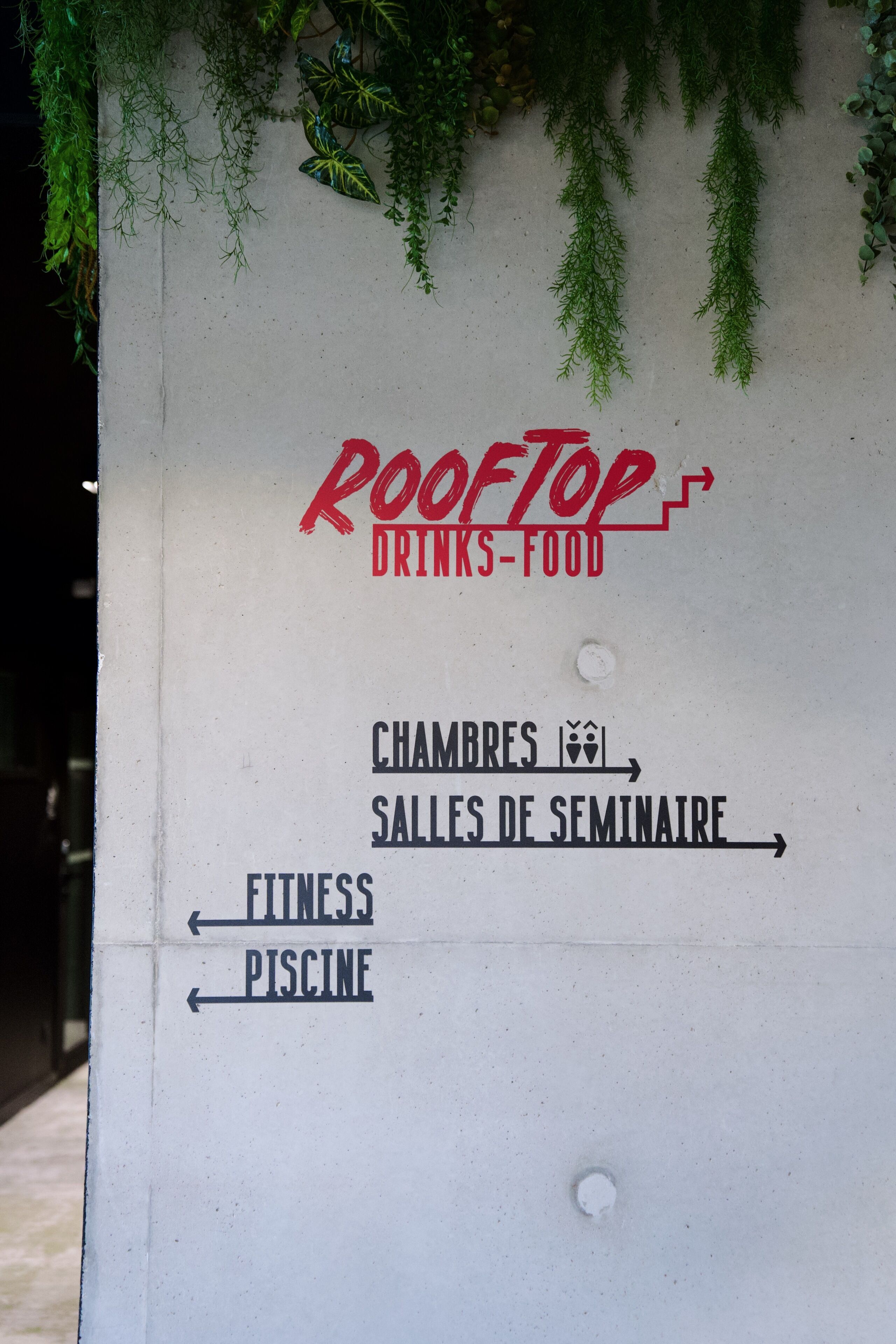 A directional sign with 'Rooftop Drinks-Food' and arrows pointing to 'Chambres 1er,' 'Salles de Seminaire,' 'Fitness,' and 'Piscine.'