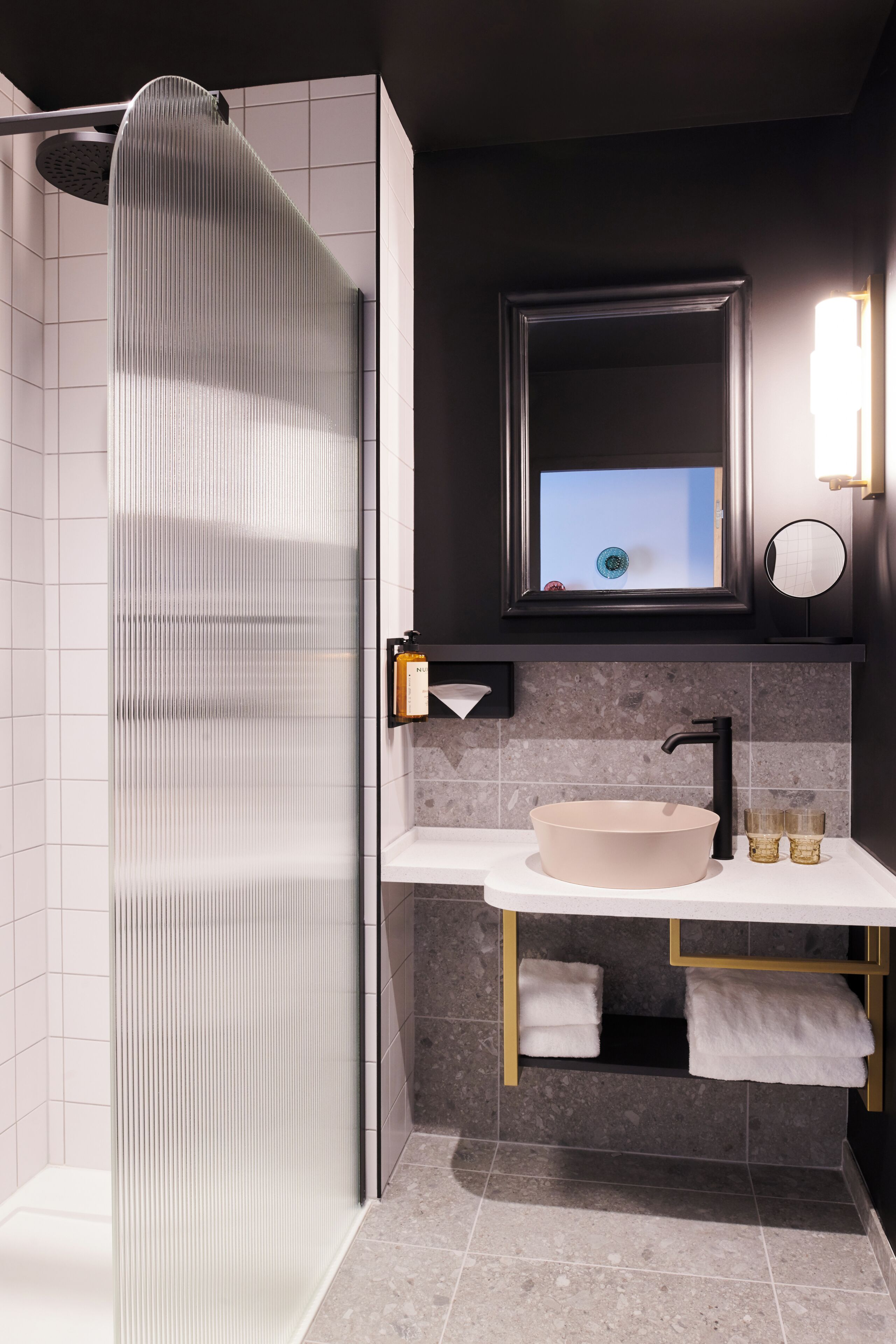 A modern bathroom with a glass shower enclosure, a round sink, and a mirror above the sink.