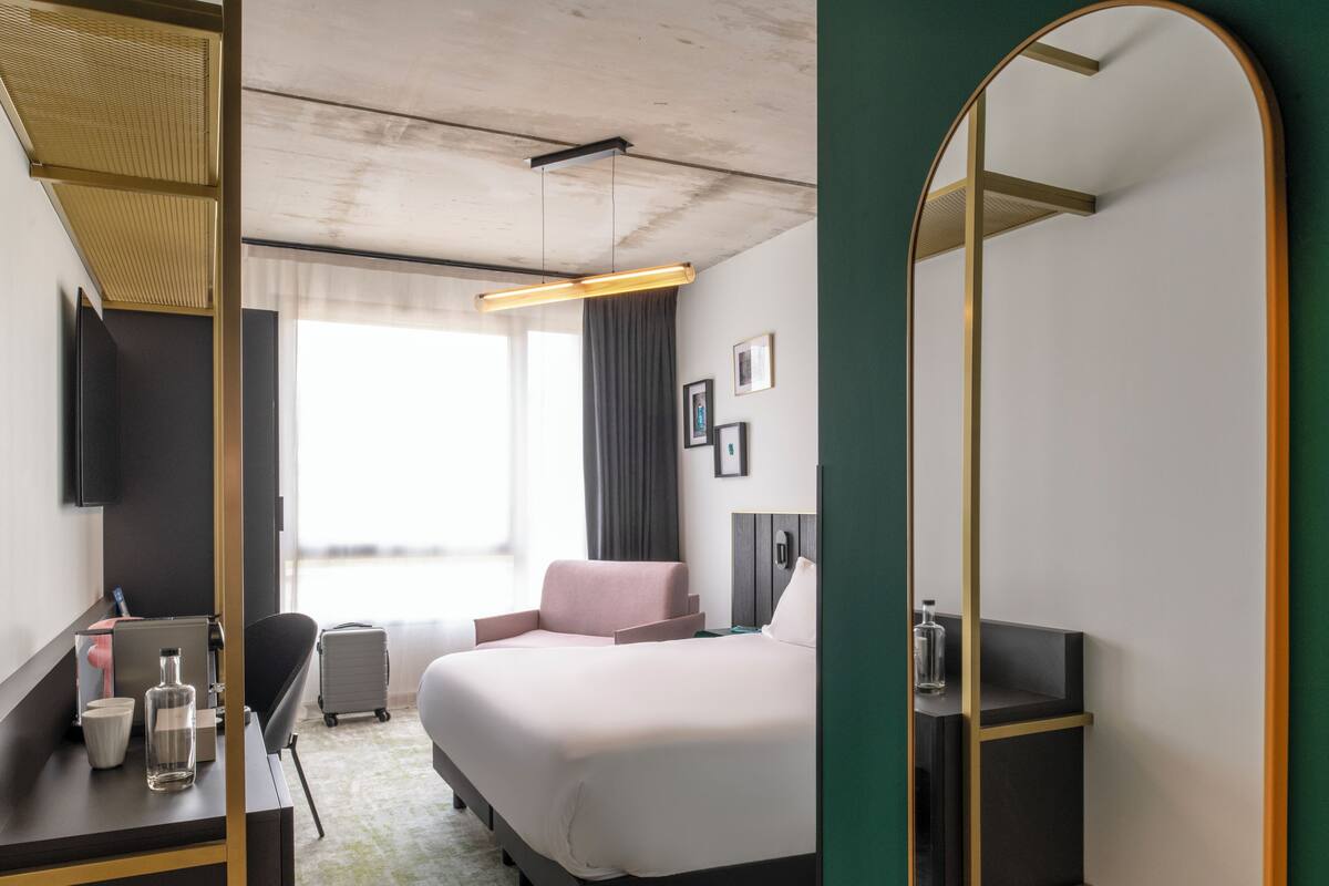 Una habitación de hotel con una cama, un escritorio con silla, un espejo y un televisor en la pared.