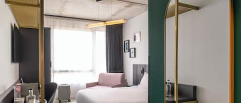 Una habitación de hotel con una cama, un escritorio con silla, un espejo y un televisor en la pared.