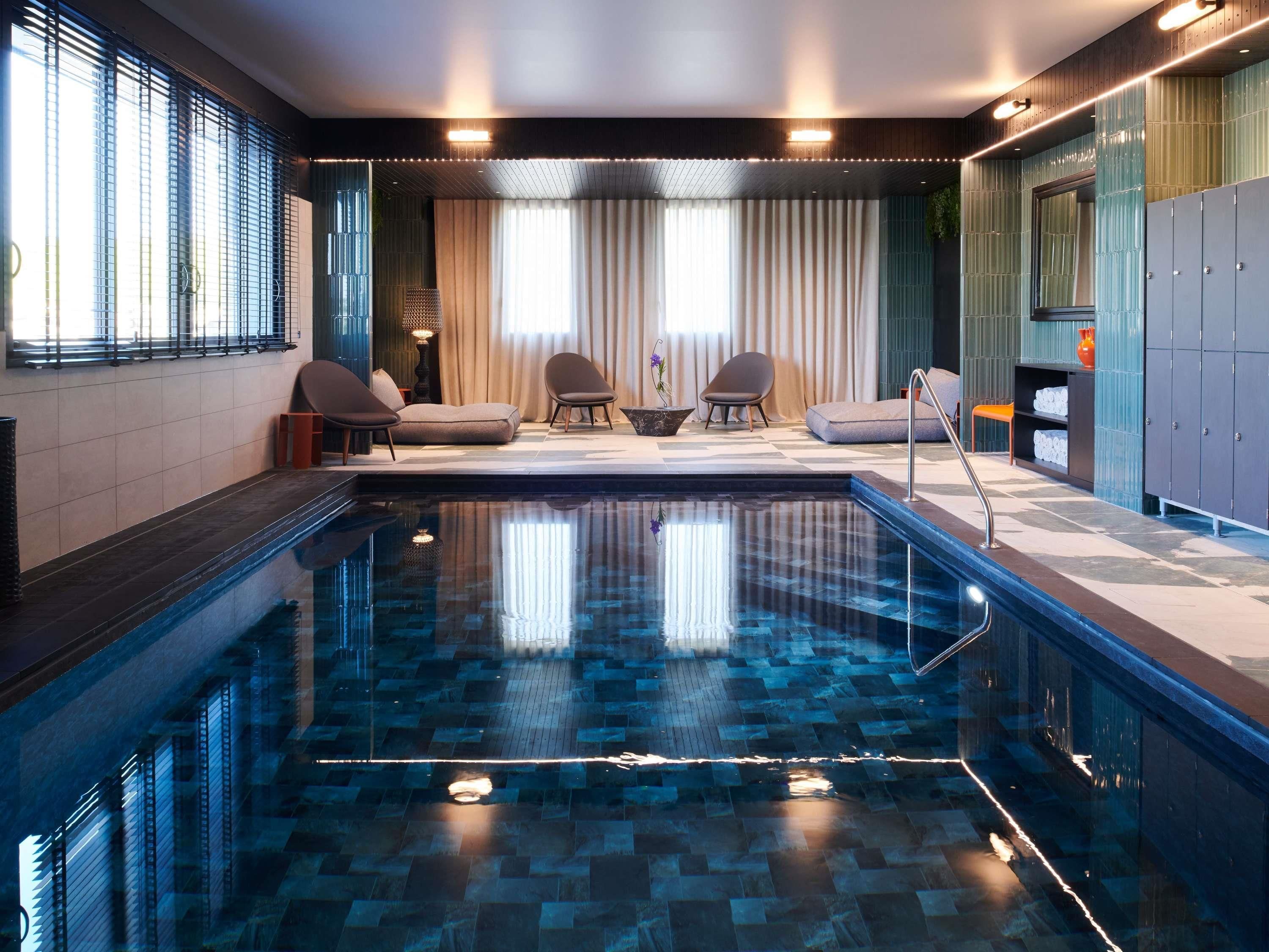 A modern indoor pool area with a checkered floor, seating, and a view of the outdoors.