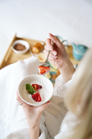 Une personne tenant un bol de yaourt aux fraises, une cuillère et un plateau sur lequel se trouvent une théière et des pâtisseries.
