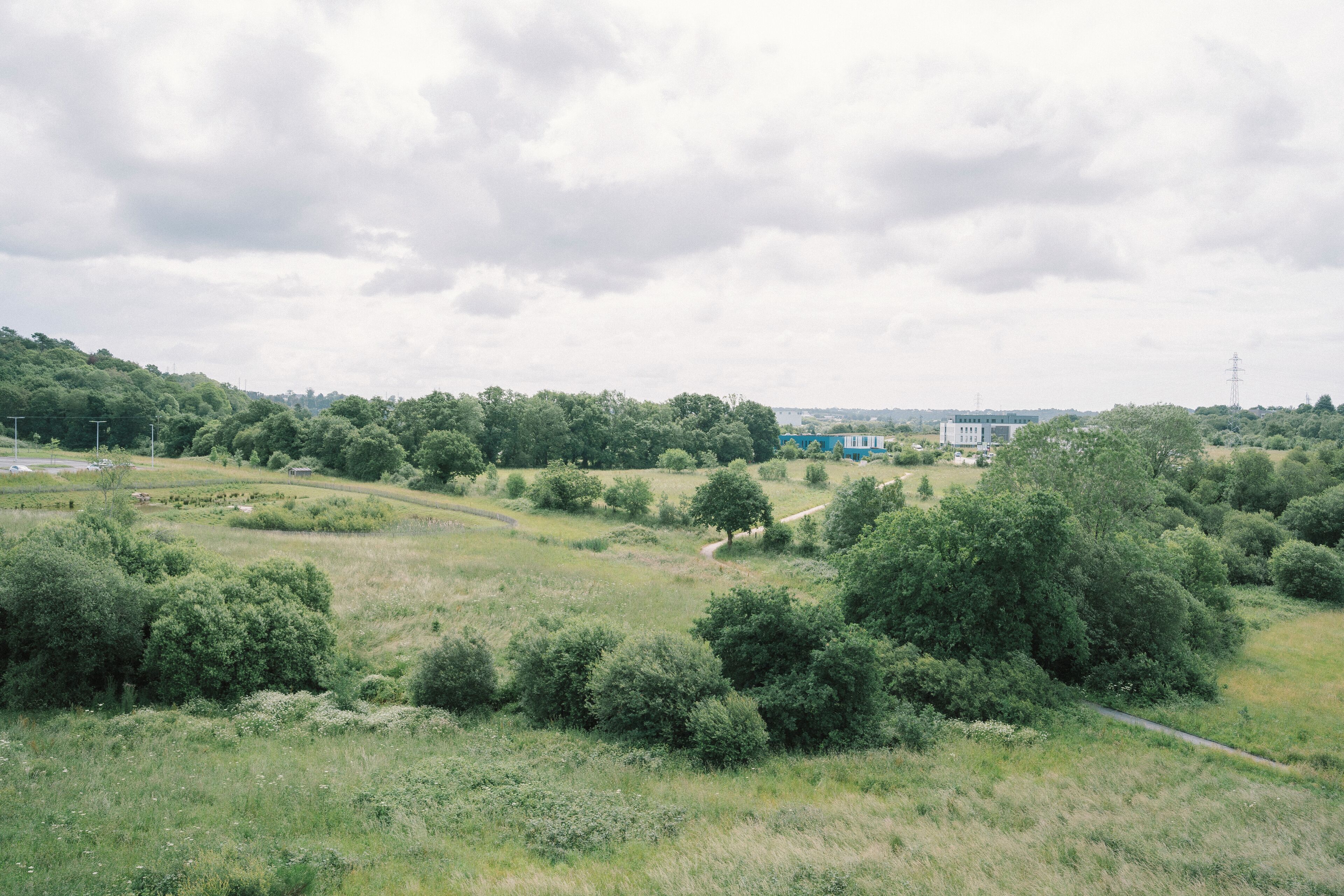 A rural landscape with rolling hills, scattered trees, and a few buildings in the distance.