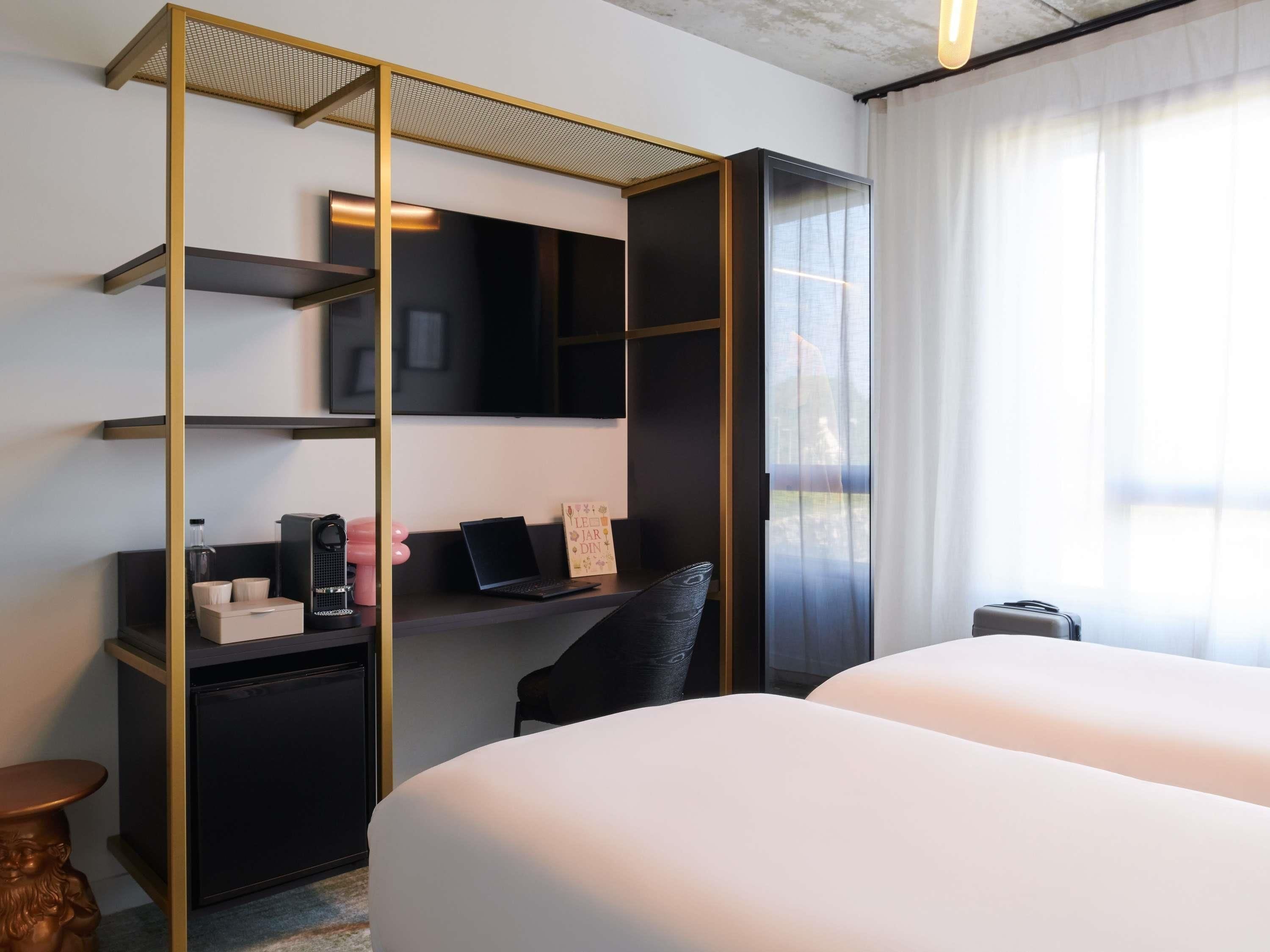 A hotel room with a bed, a desk with a computer, a TV, and a window with curtains.