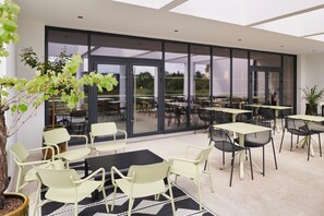 Un espace extérieur aménagé en terrasse, avec des tables et des chaises, de grandes portes vitrées et une plante en pot.