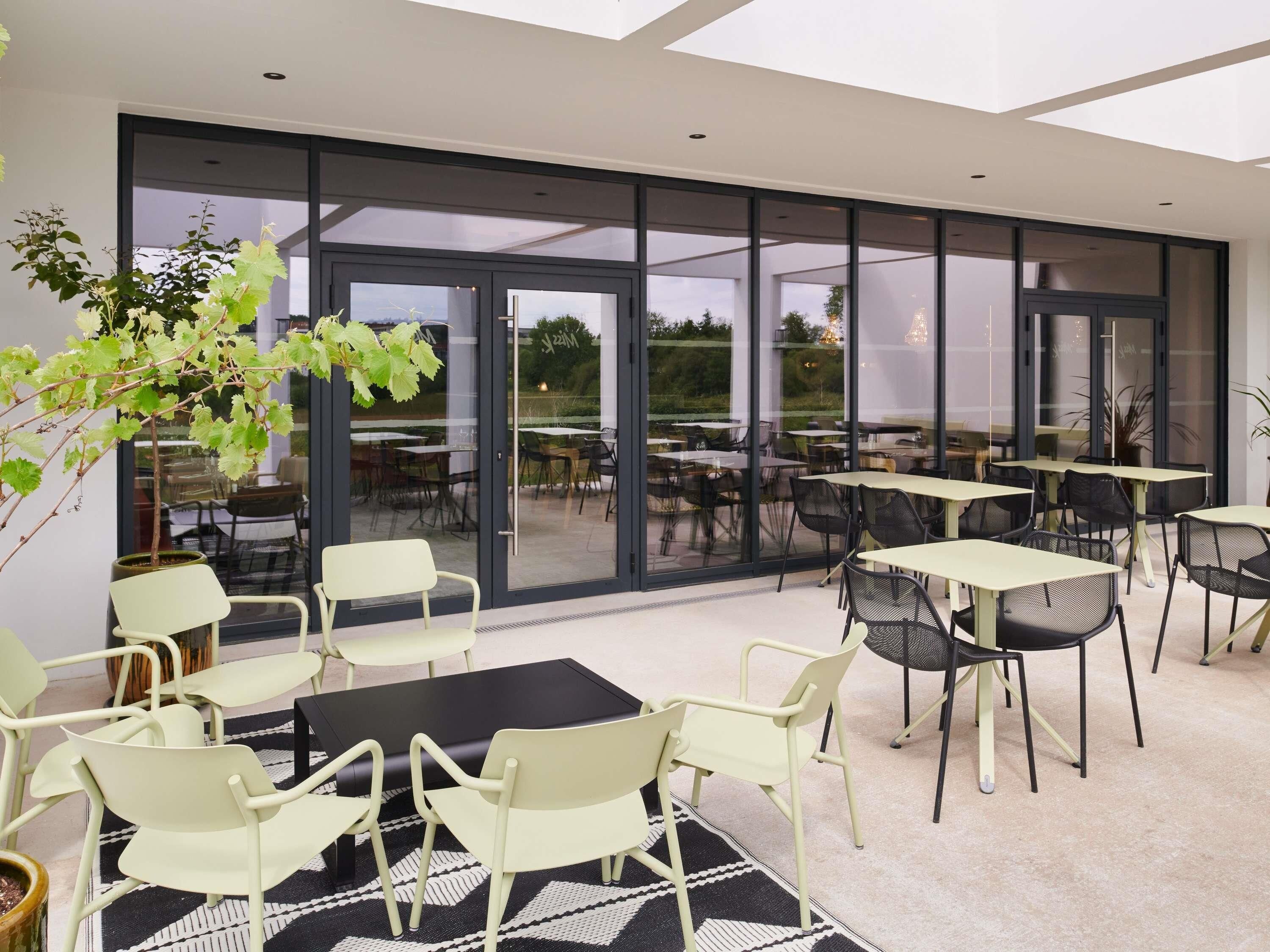 A modern outdoor dining area with glass doors, tables, and chairs.