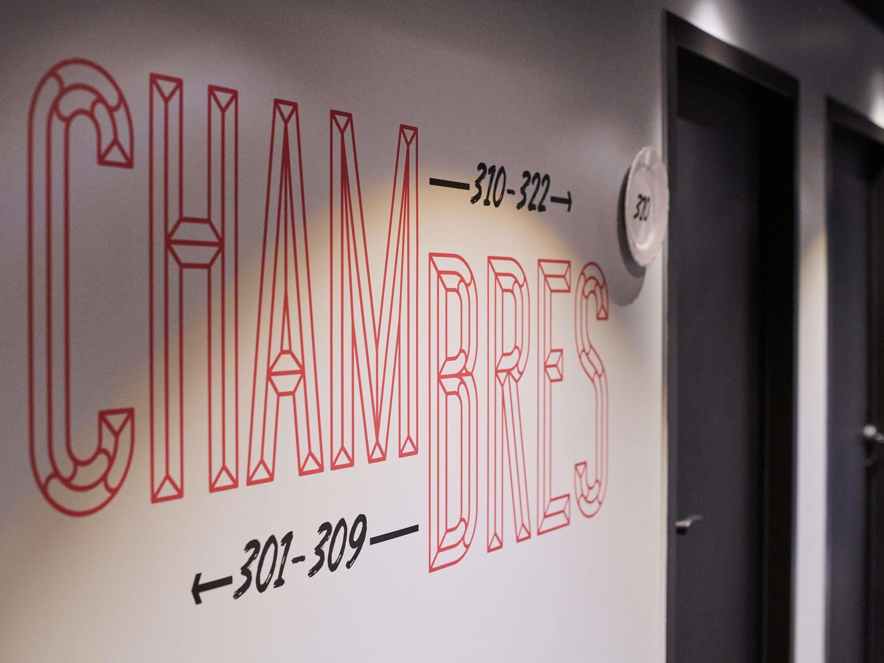 Una pared con el nombre 'CHAMBRE' y dos números de teléfono '310-322' y '301-309' en una tipografía estilizada.