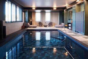 Un espace piscine intérieur moderne, doté d’une piscine à eau claire, de sièges disposés autour de la piscine et offrant une vue sur l’extérieur.