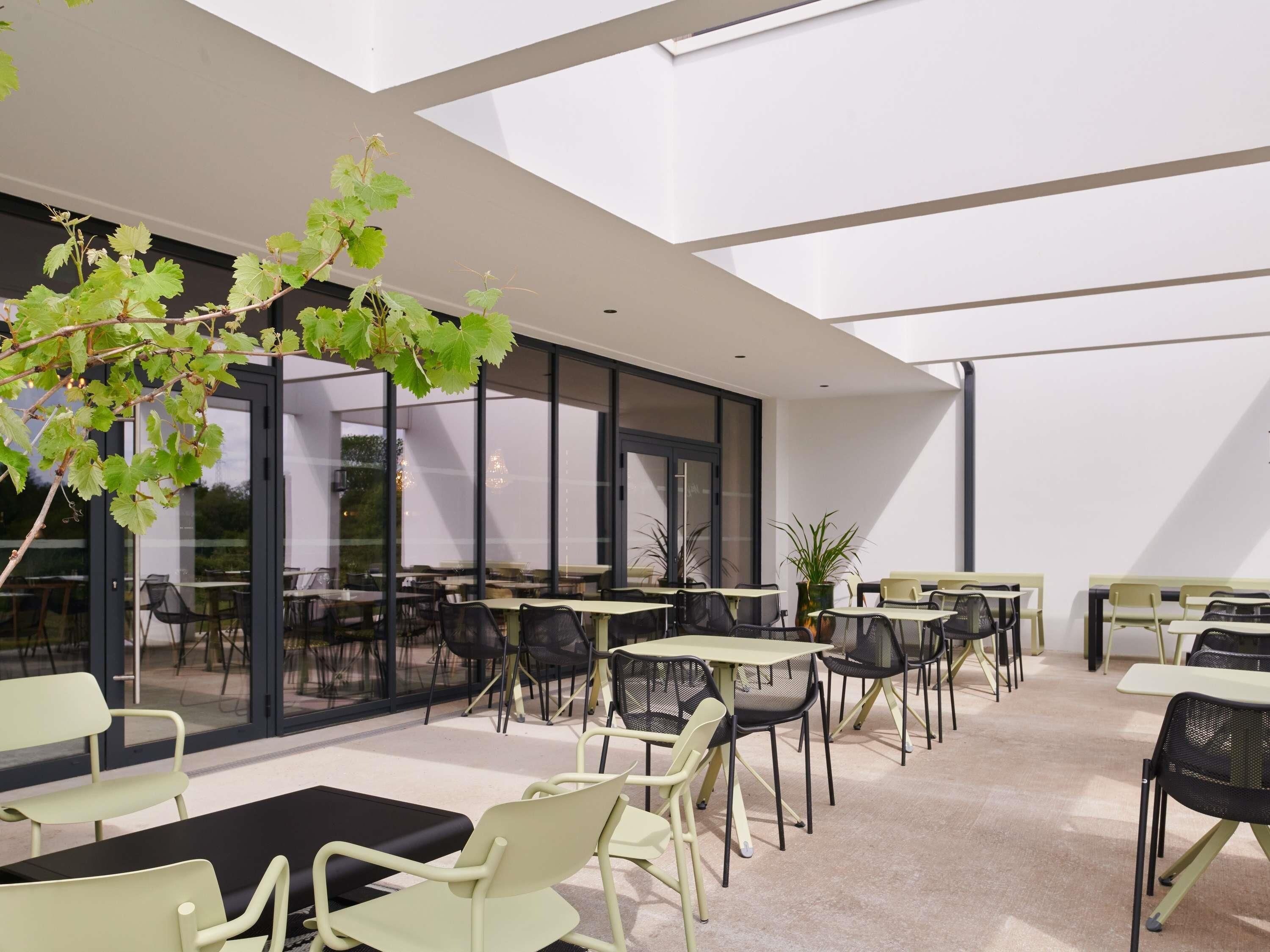 An outdoor seating area with tables and chairs, large windows, and a view of the surrounding area.