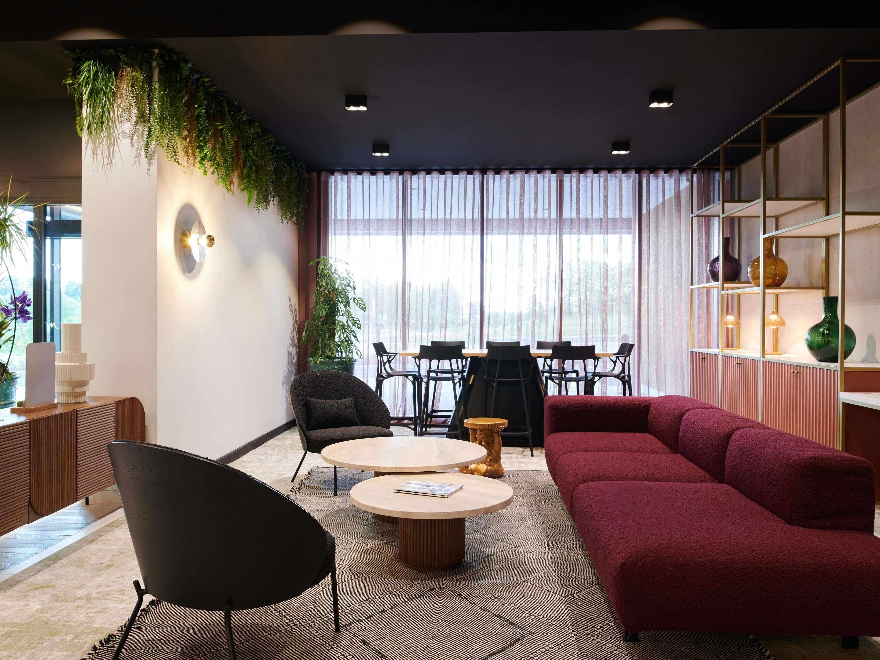 A modern living room with a red sofa, black chairs, a round coffee table, and a dining area with a table and chairs.