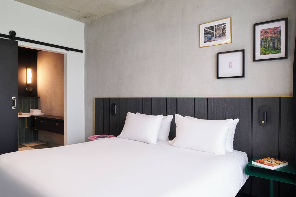 Una habitación de hotel moderna con una cama, una mesita de noche y una pared decorada con cuadros.