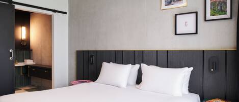 A modern hotel room with a bed, bedside table, and a wall with framed pictures.