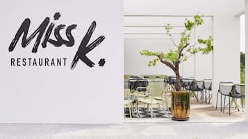 Une enseigne de restaurant portant le nom « Miss K. » et un espace avec des tables et des chaises où les clients peuvent s’asseoir.