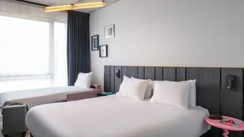 A hotel room with two beds, a desk, a chair, a suitcase, a magazine, and a window with curtains.