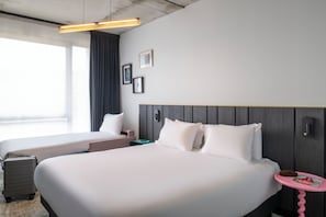Ein Hotelzimmer mit zwei Betten, einem Schreibtisch, einem Stuhl, einem Koffer, einer Zeitschrift und einem Fenster mit Vorhängen.