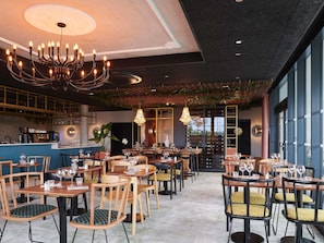 Interior de restaurante con varias mesas y sillas, una zona de bar y un candelabro.