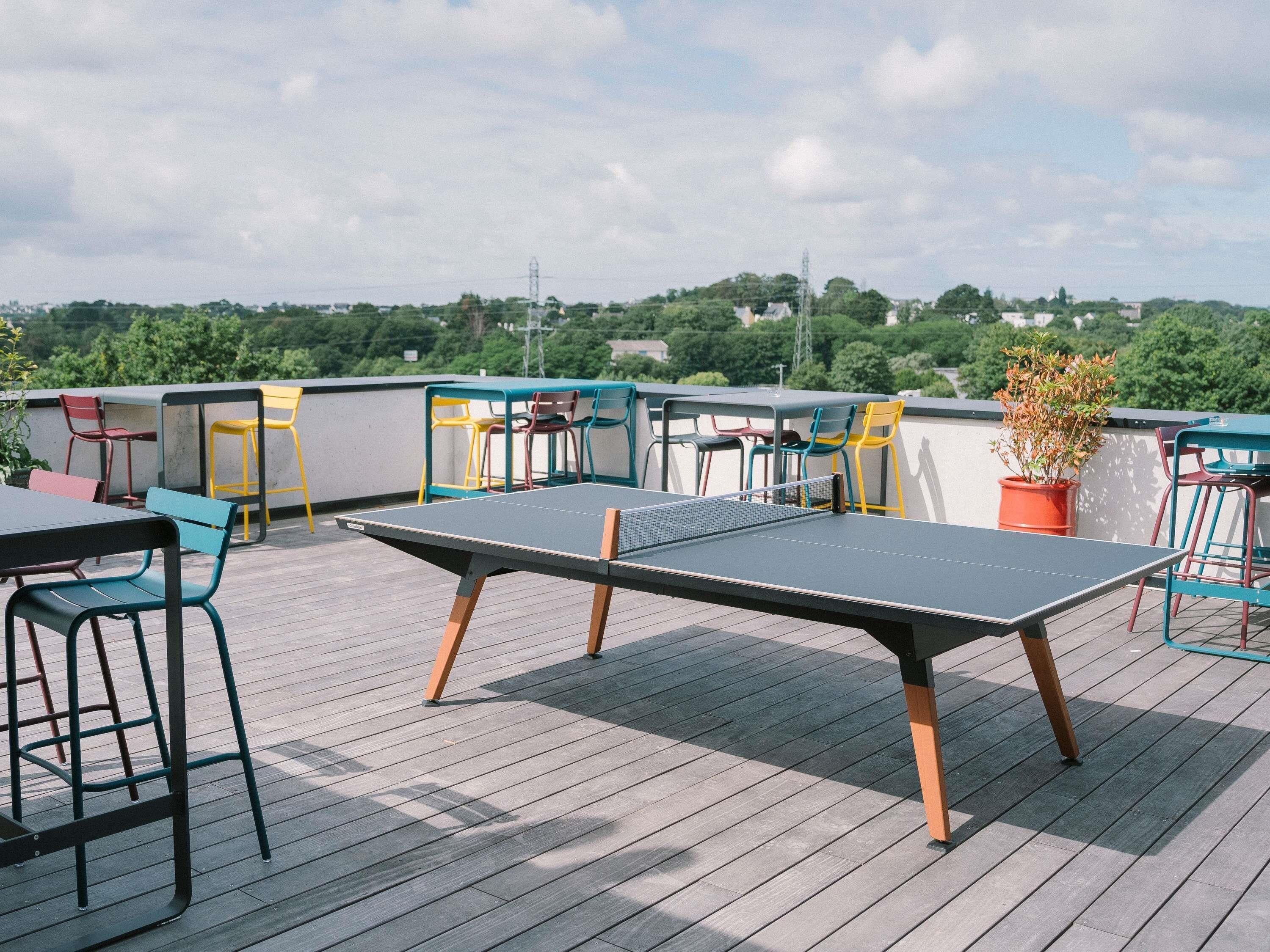 A rooftop terrace with a ping pong table, chairs, and a potted plant.