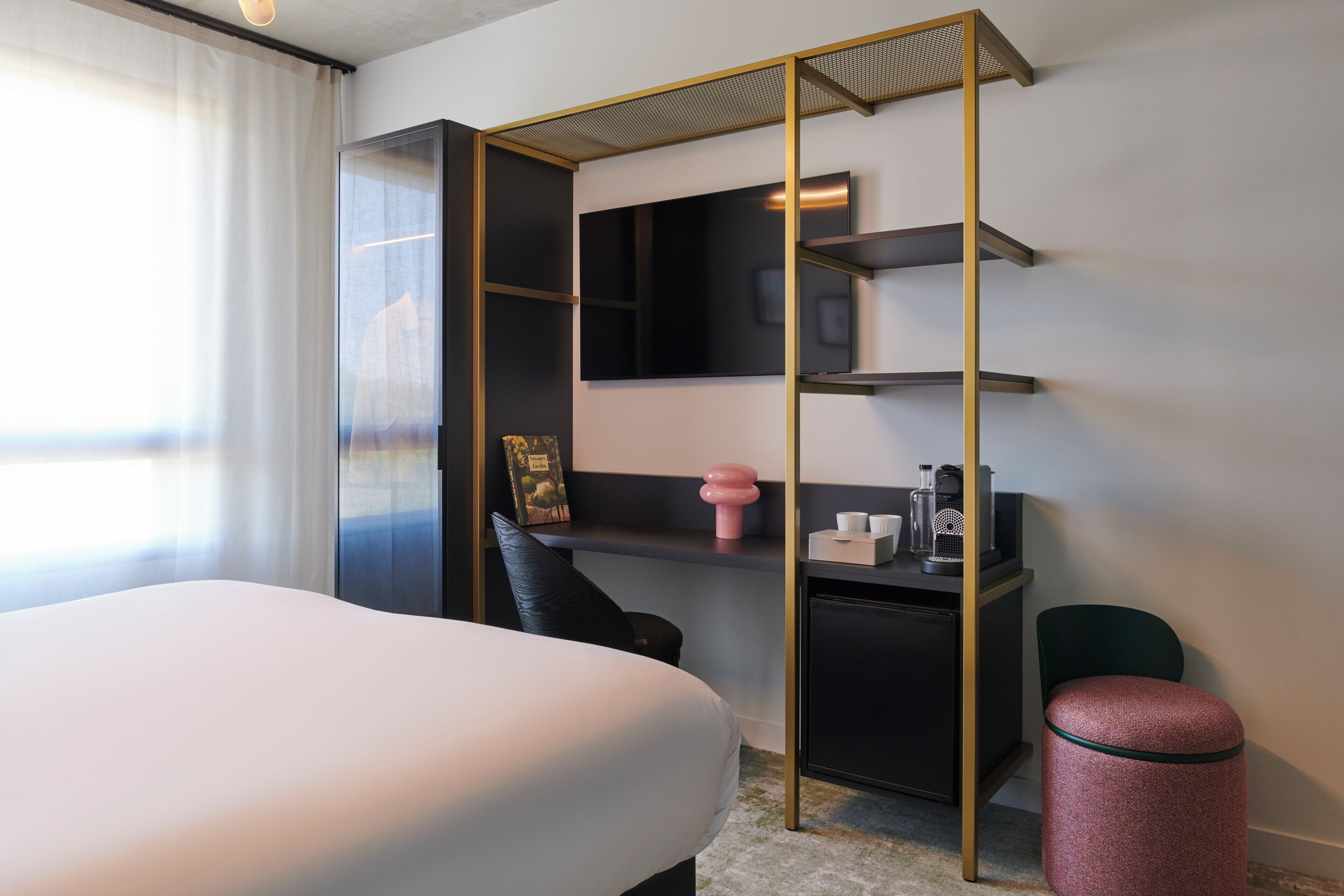 A hotel room with a bed, a desk with a computer, a chair, and a small trash bin.