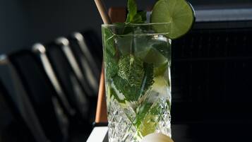A glass of a beverage with mint and lime, placed on a table with a laptop and a smartphone.