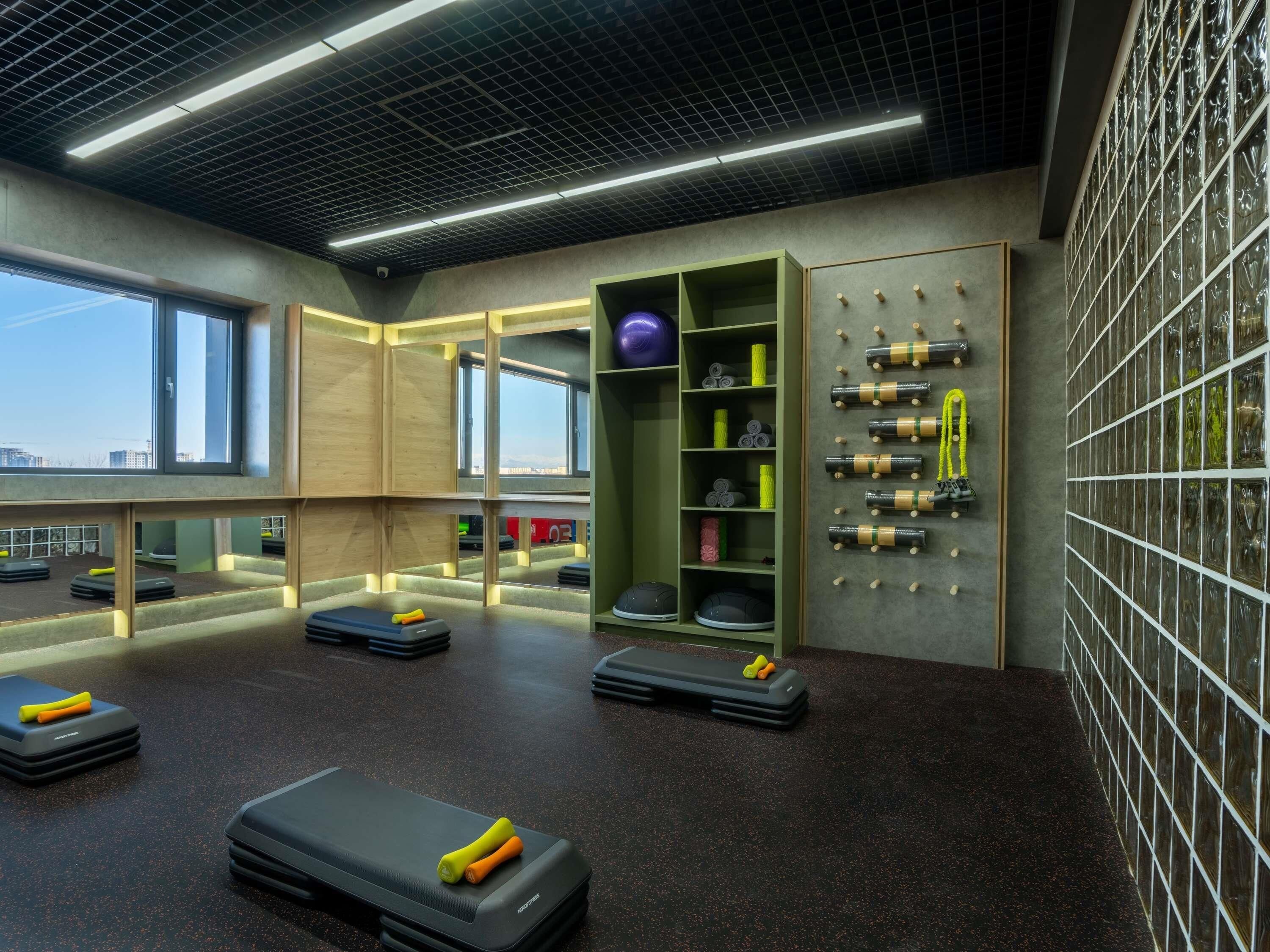 Un gimnasio moderno con equipo de ejercicio, un estante de pared y amplias ventanas.