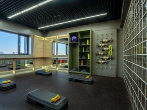 A modern gym with exercise equipment, a wall-mounted storage unit, and large windows. - Mercure Tashkent North (Tashkent)